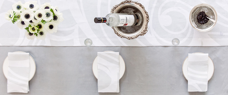Huddleson silvery grey linen tablecloth and swirling Slaon napkins and table runner with white anemones, caviar and Kettel One vodka