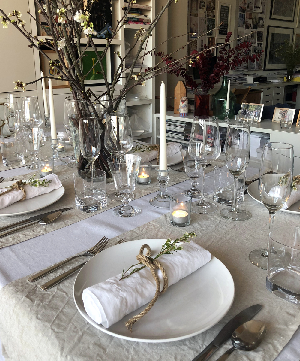 Scandinavian dinner party layering white and natural flax table linens, candles and blossom